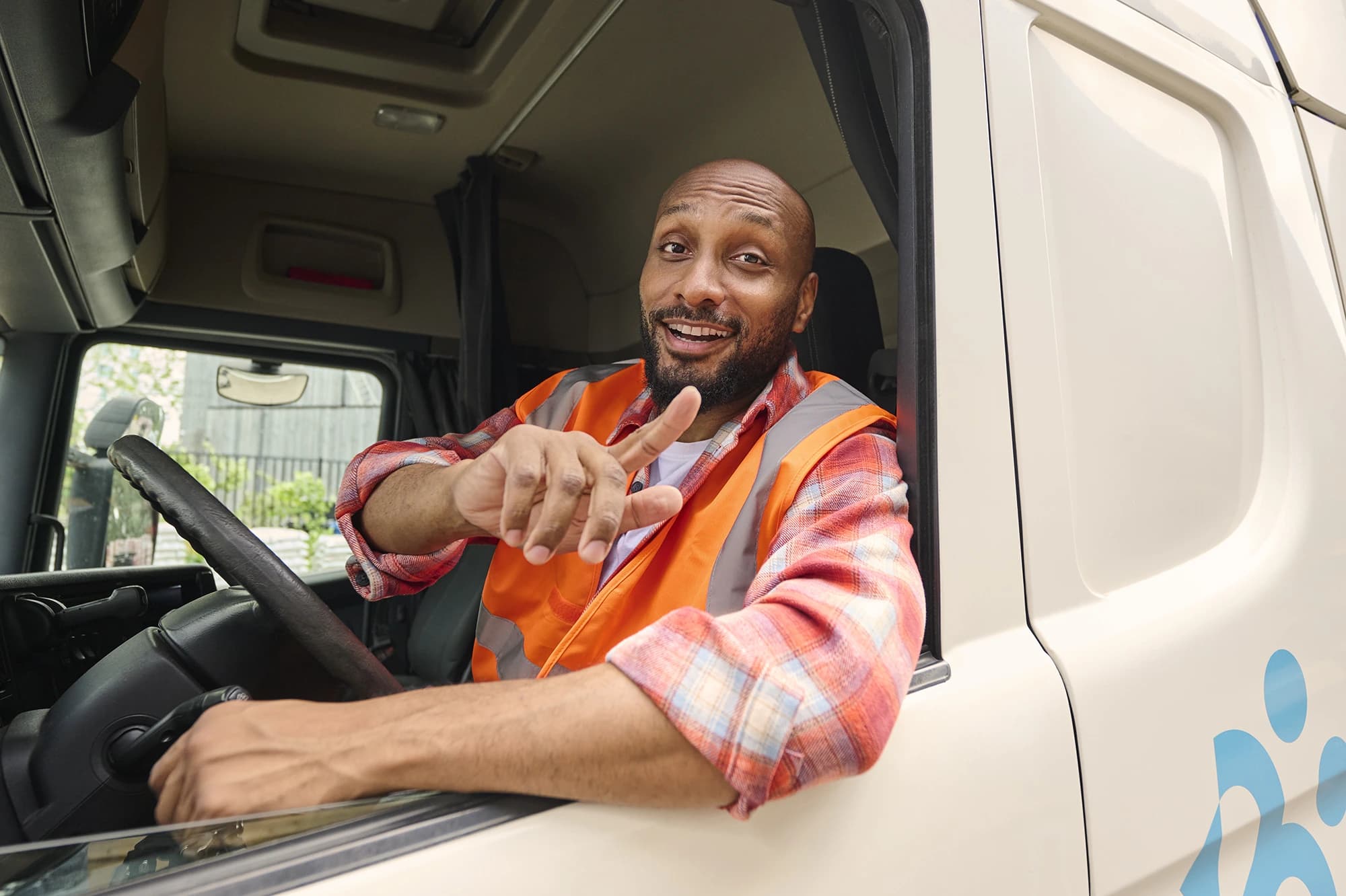 Vrachtwagenchauffeur in fluovest glimlacht en wijst vanuit cabine — transportjobs via Accent